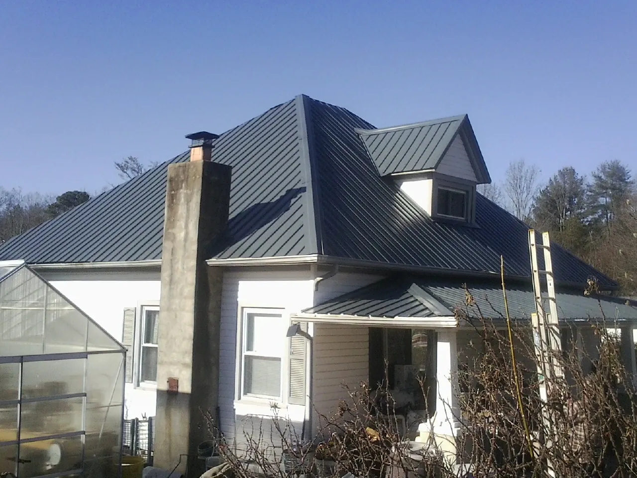 Dark blue standing seam metal roof on a white farmhouse with dormer — Slate & Tile Roof Repair by Roofing Brothers in Tie Siding