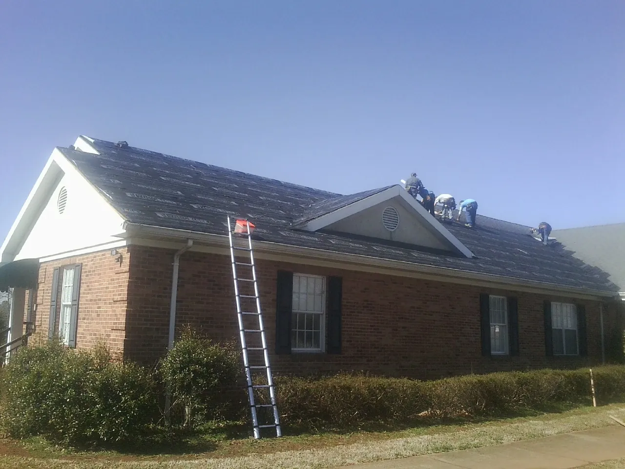 Crew tearing shingles off a brick ranch roof with a ladder set — Metal Roof Repair work by our crew in Tie Siding