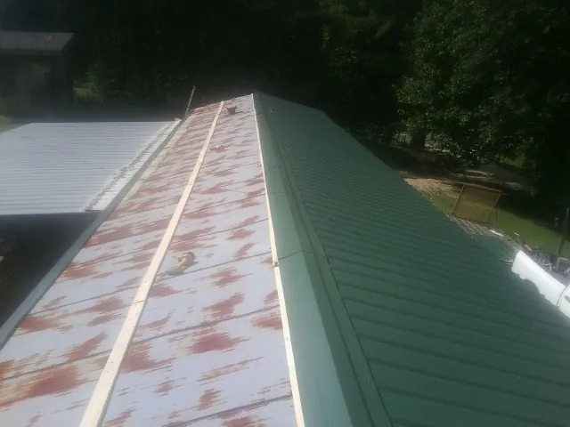 Old rusted panels beside newly installed green metal roofing — Wind Damage Roof Repair by Roofing Brothers in Tie Siding