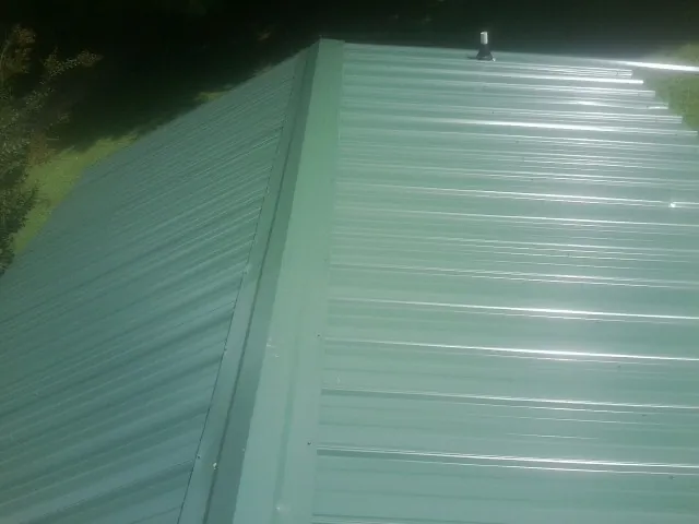 New green metal panels meeting at the ridge of a roof — Flat Roof Repair work by our crew in Tie Siding