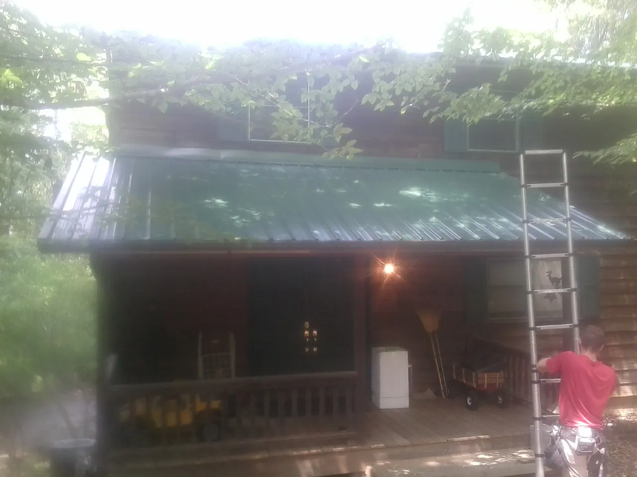 Worker on a ladder at the green porch roof of a wooded cabin in Tie Siding