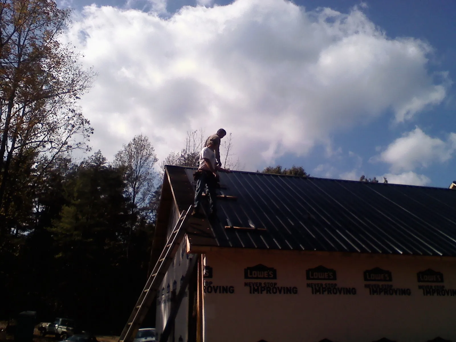 Roofer fastening dark metal panels high against a cloudy sky, from a Roof Inspection job in Tie Siding