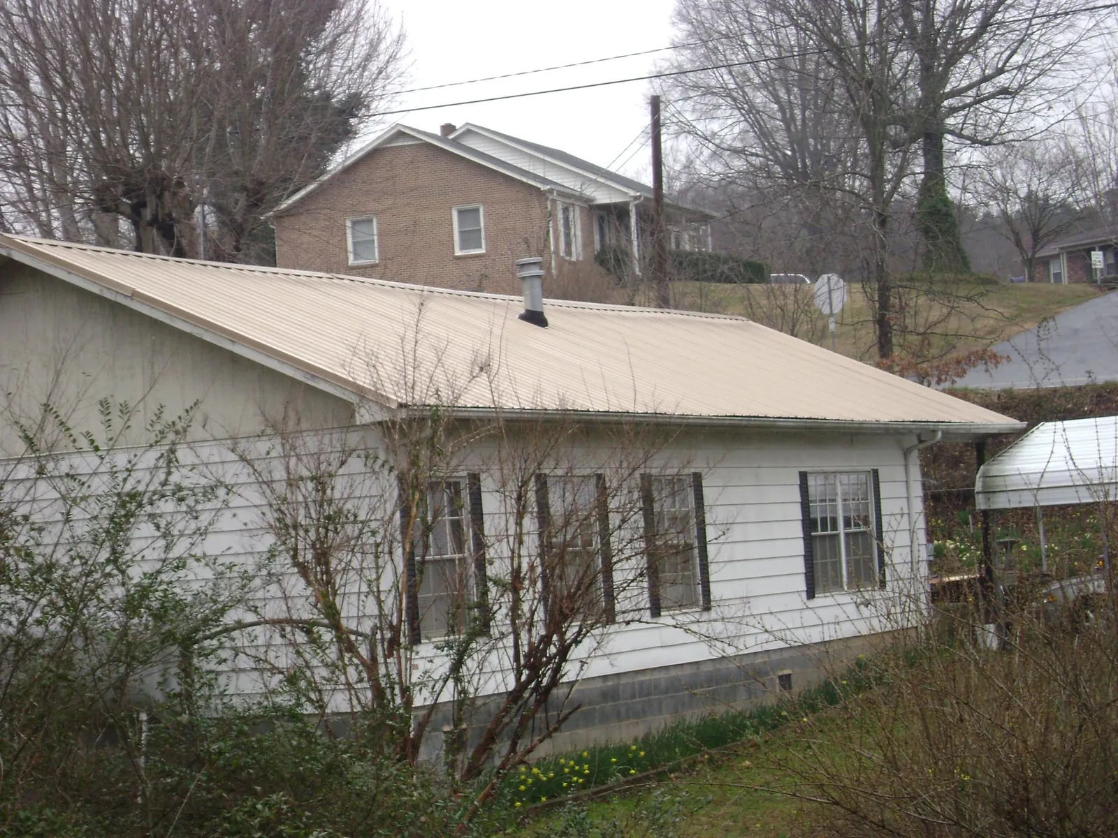 Tan metal roof on a white sided house set into a hillside — Commercial Roofing by Roofing Brothers in Tie Siding