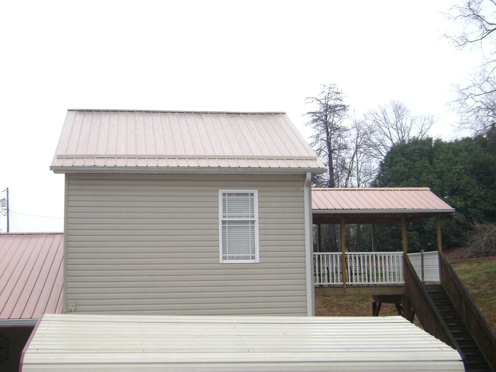 Tan metal roofs on a two story addition and attached porch, from a Roof Replacement job in Tie Siding