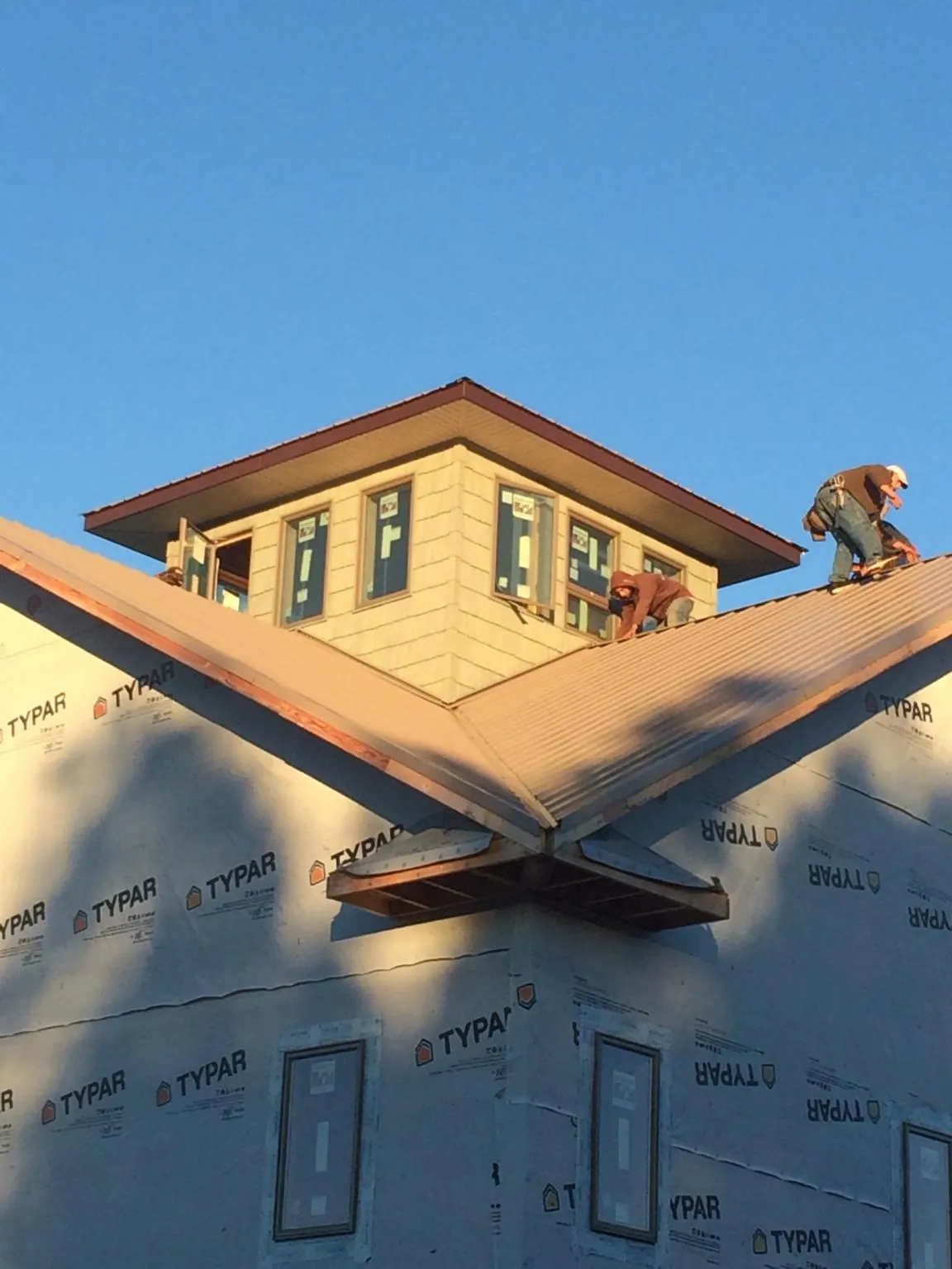 Roofers working around a rooftop cupola on a new metal roof at sunset — Roof Waterproofing in Tie Siding by Roofing Brothers